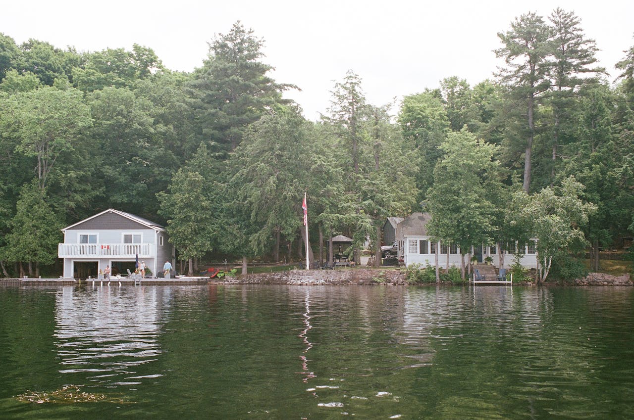 Tranquil scene of lakeside houses surrounded by lush forest and calm waters, ideal for relaxation and tourism.